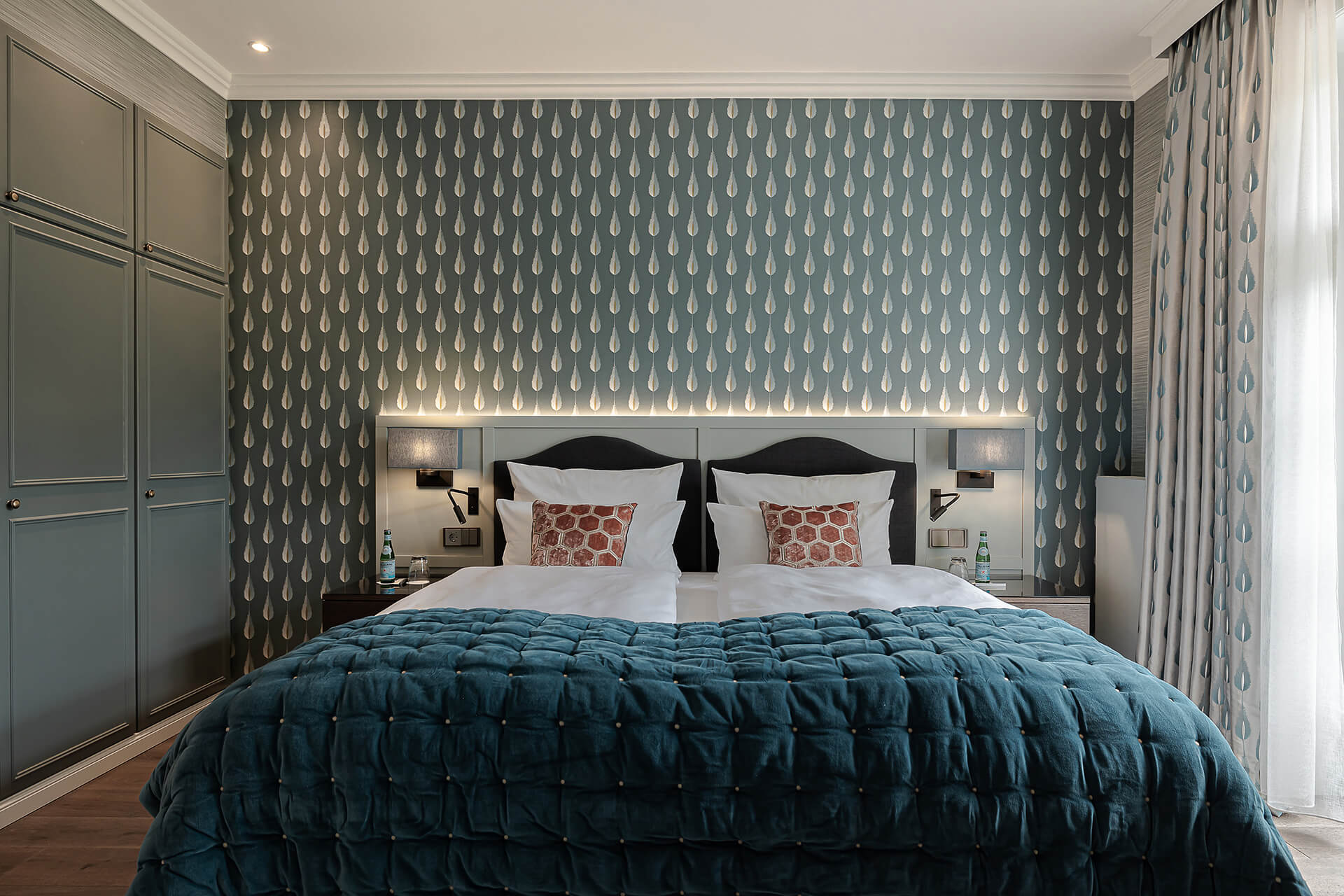 Ein Bett mit einer blauen Decke und einer weißen Lampe an der Wand. Suite Unsere Suiten sind ein wa
